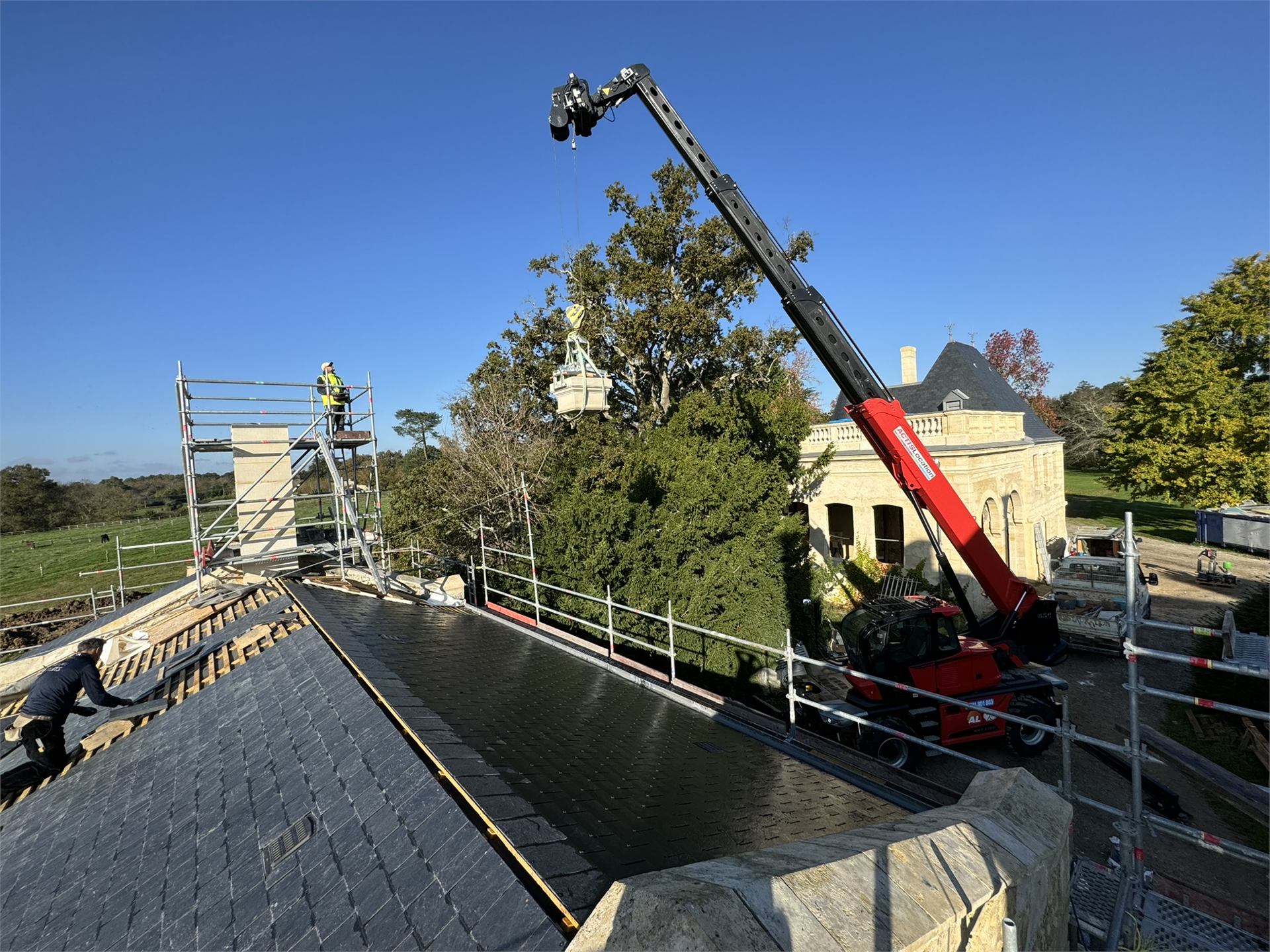 Pose d'une cheminée en pierre taillée à la grue, chantier de maçonnerie traditionnelle